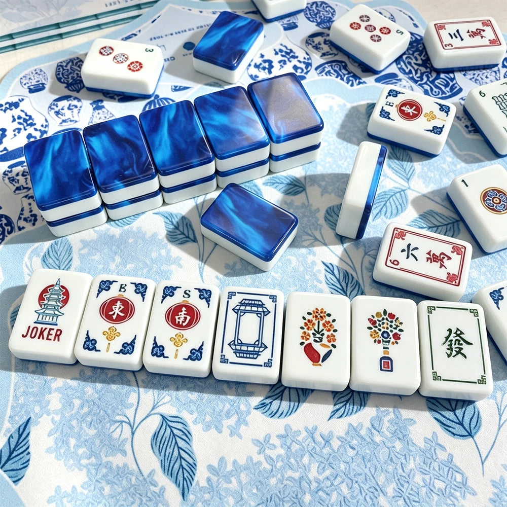 Blue marbled acrylic Mahjong tiles arranged in a wall beside hand-illustrated wind, joker and flower tiles on a blue floral mat