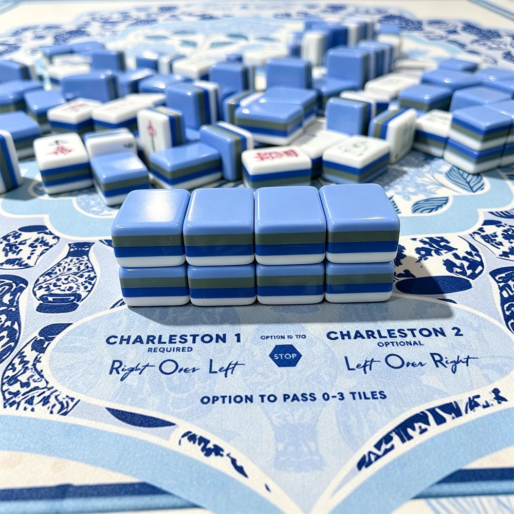 Blue and white striped acrylic Mahjong tiles stacked on a chinoiserie-patterned scorecard mat with Charleston passing instructions