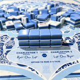 Blue and white striped acrylic Mahjong tiles stacked on a chinoiserie-patterned scorecard mat with Charleston passing instructions