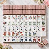 Rows of American mahjong tiles with pink and white artwork arranged on a table