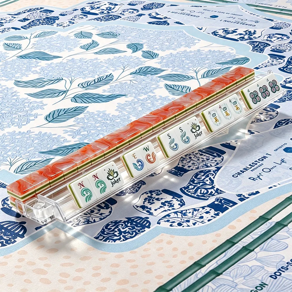 Coral marbled acrylic Mahjong tiles with hand-illustrated wind and joker tiles arranged in a clear tile rack on a blue chinoiserie mat