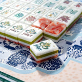 Green and red marbled acrylic Mahjong tiles with hand-illustrated joker and floral wreath motifs arranged on a blue chinoiserie mat