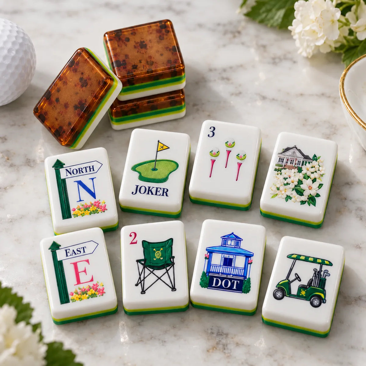 Golf-themed American mahjong tiles with North and East wind tiles, golf green joker, golf cart and clubhouse designs beside amber tortoiseshell tile backs on a marble table