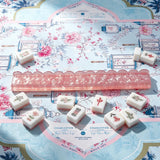 Pink acrylic mahjong tile pusher displayed with mahjong tiles on a decorative game table
