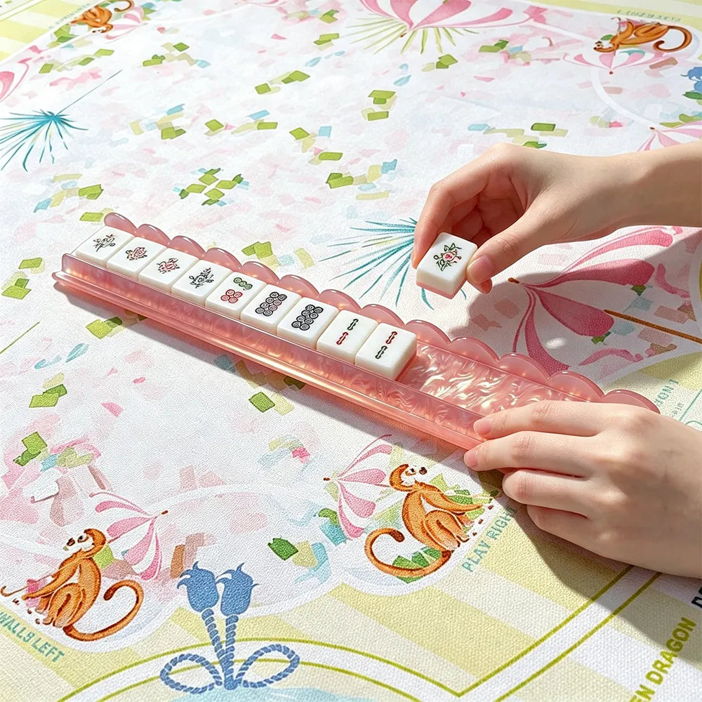 Pink acrylic mahjong tile pusher in use with arranged mahjong tiles on a decorative table